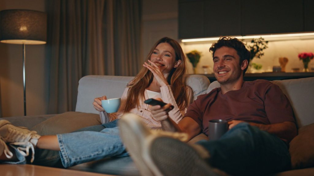 A couple relaxing on a couch, watching TV together in the evening