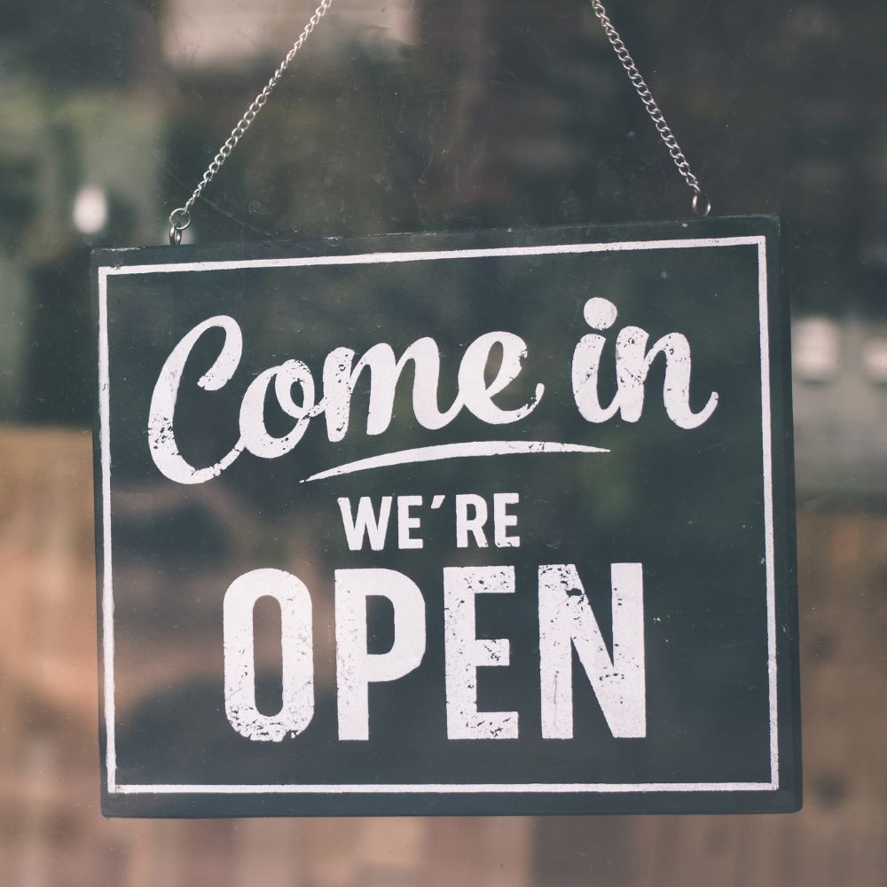 A black-and-white ‘Come in, we’re open’ sign hanging in a shop window